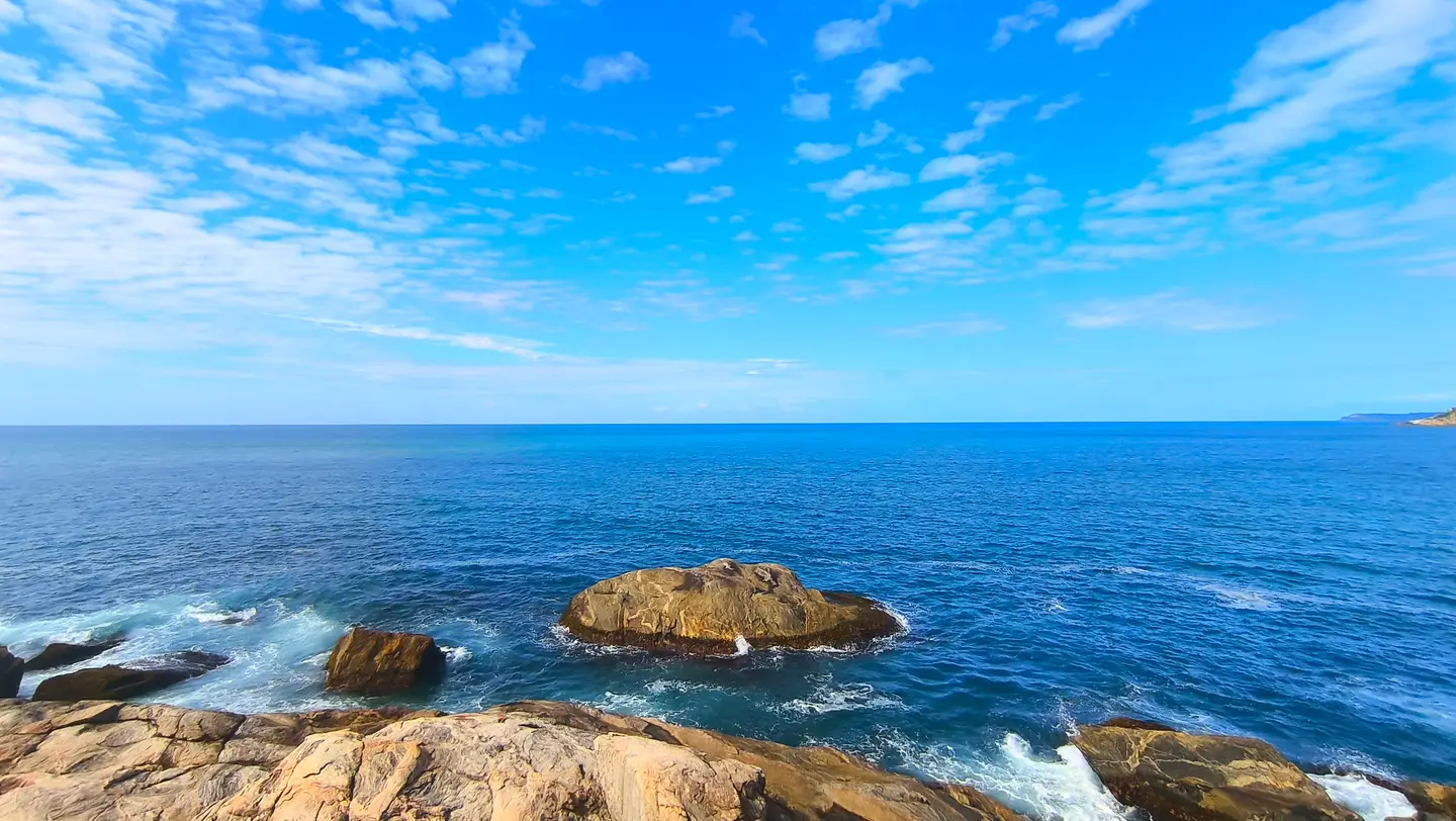 Rocky coast and blue sea under a cloudy sky.